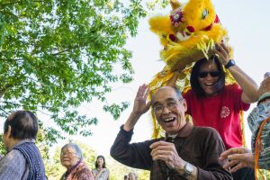 a man smiling and a woman carrying a lion behind him